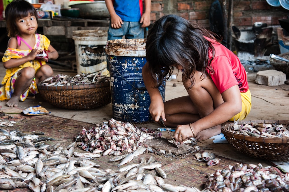 woman in red tank top sitting on ground with dried fish during daytime