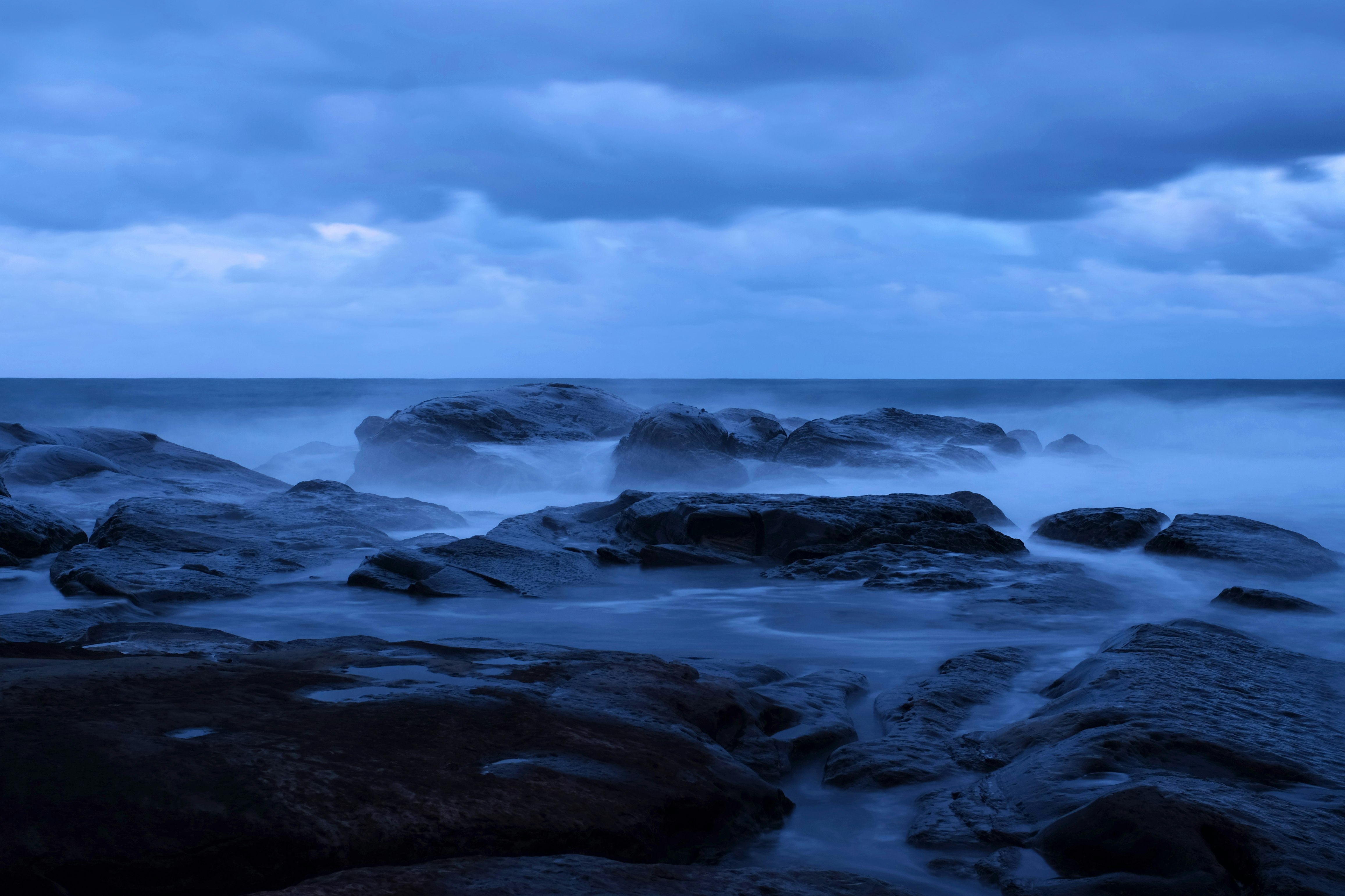 ocean waves crashing on rocks under white clouds and blue sky during daytime