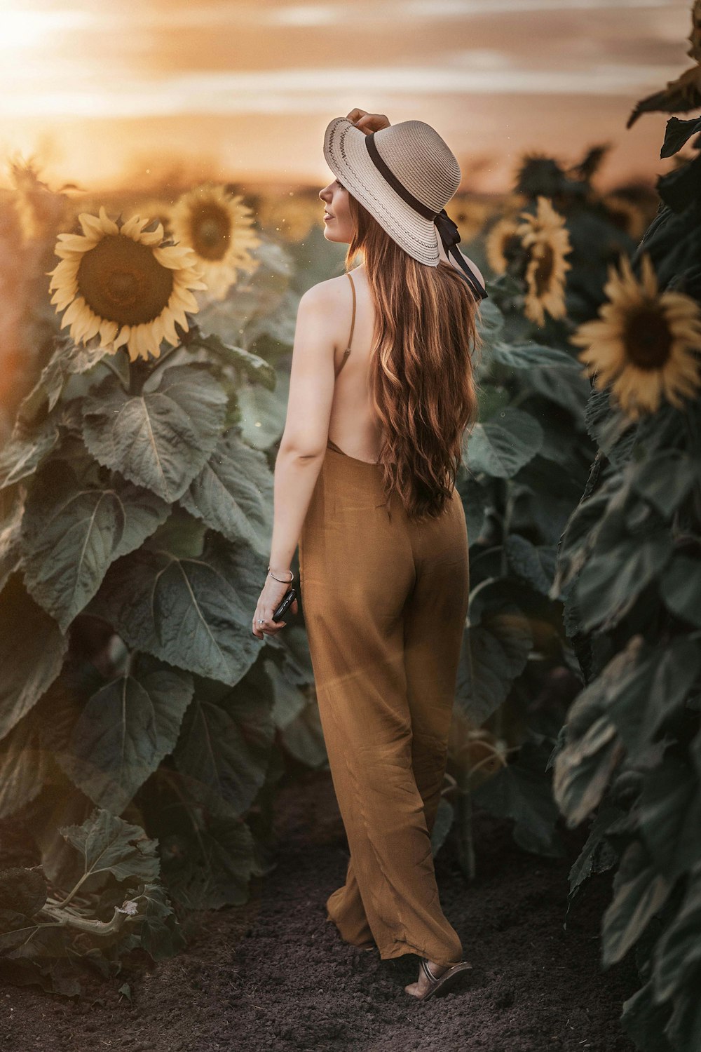 Frau in braunem ärmellosem Kleid tagsüber auf Sonnenblumenfeld stehend