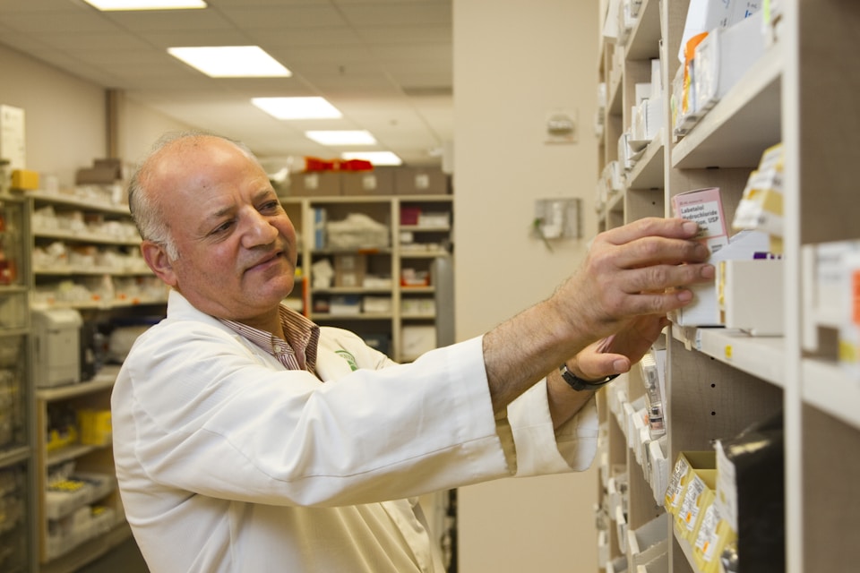 An older male pharmacist taking medication off of a shelf