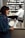 A woman wearing a blue sweater and scarf is looking at a piece of paper with a drawing on it. In the background, a pharmacist in a white coat is working behind the counter, which is filled with numerous medicine bottles. A sign on the counter reads 'If you really want to quit.'