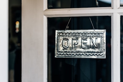 A metallic open sign with intricate patterns hangs on the glass pane of a door.