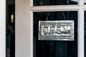 A metallic open sign with intricate patterns hangs on the glass pane of a door.