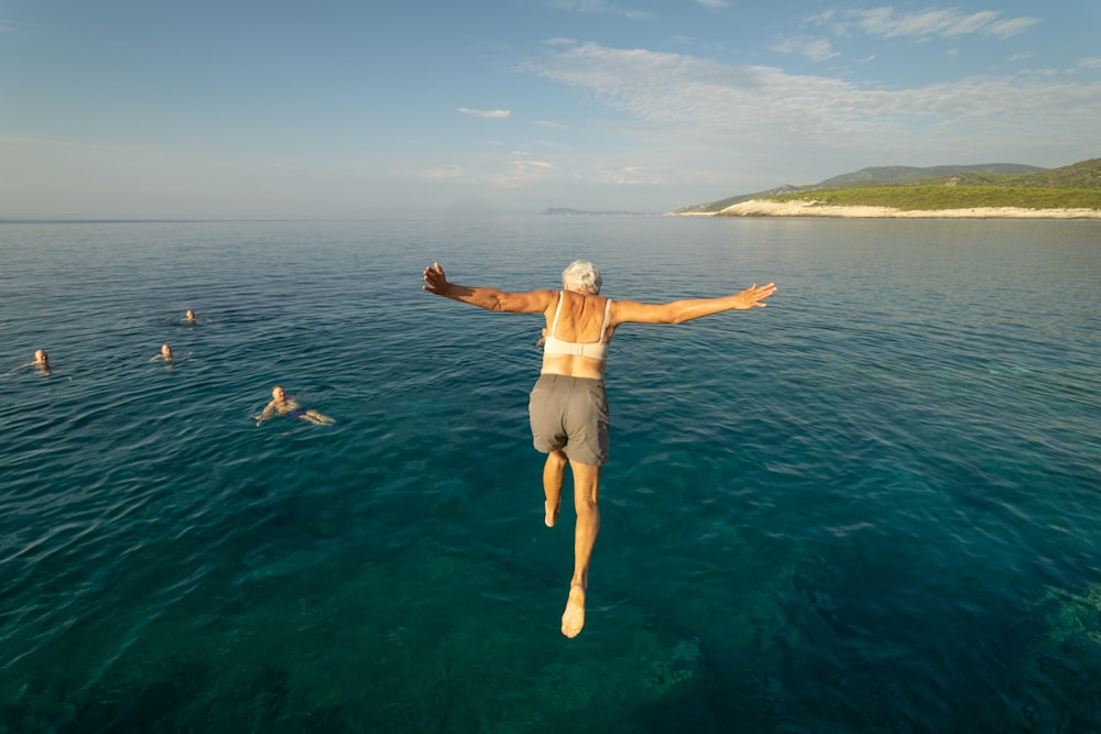 woman in white shorts jumping into the sea during daytime