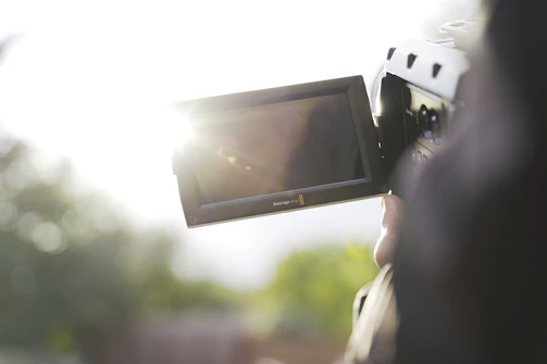 A close-up of a filmmaker reviewing footage outdoors, capturing light reflections on the camera lens.