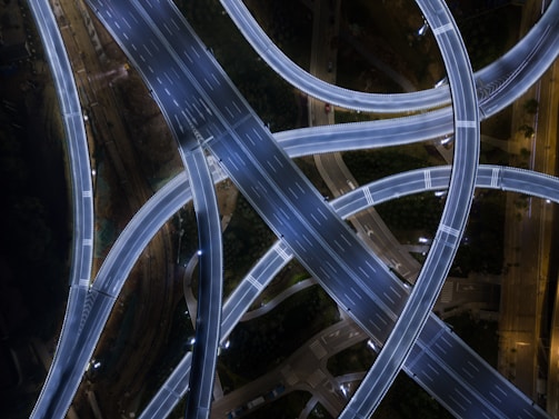 An intricate overhead view of a network of illuminated highways and overpasses at night, creating an intricate, woven pattern.