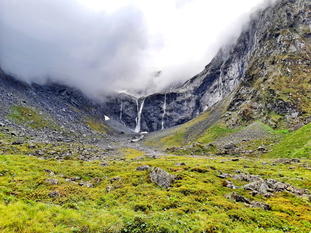 Grünes Grasfeld in Bergnähe tagsüber unter weißen Wolken