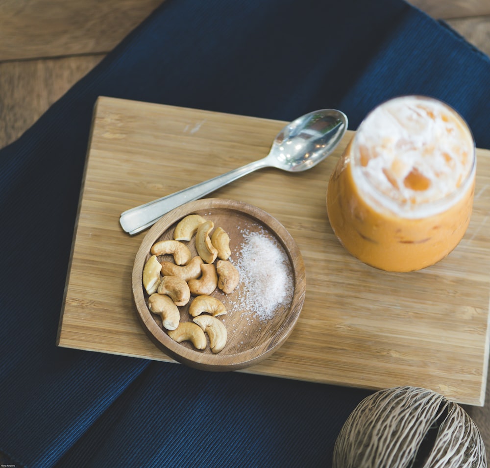 brown peanuts on brown wooden bowl beside stainless steel spoon