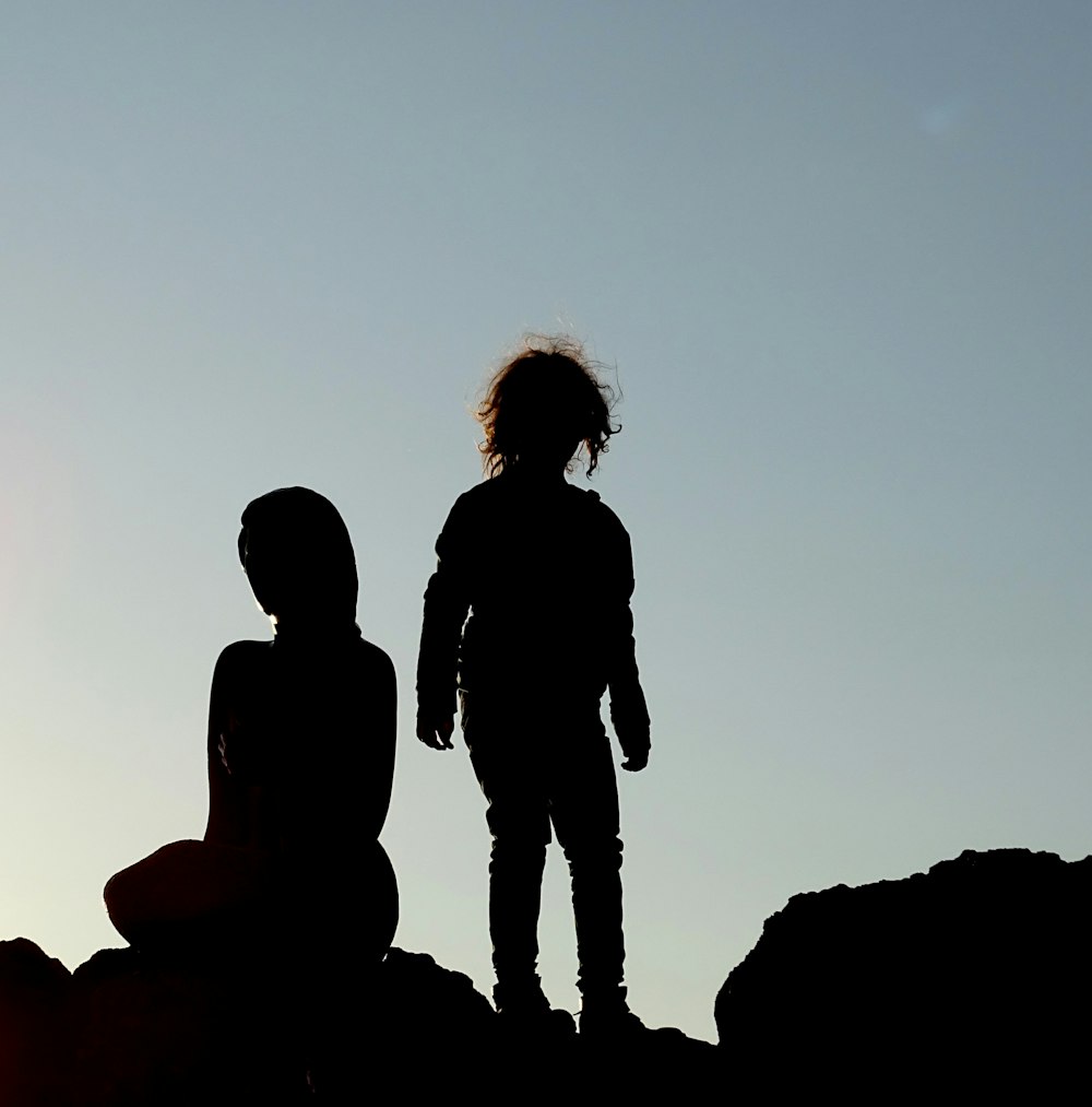 silhouette of couple standing on rock during sunset