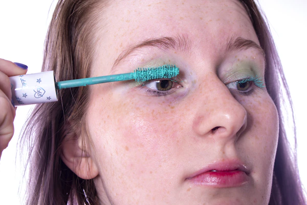 A model applying mascara with a focused expression, highlighting long, voluminous lashes.