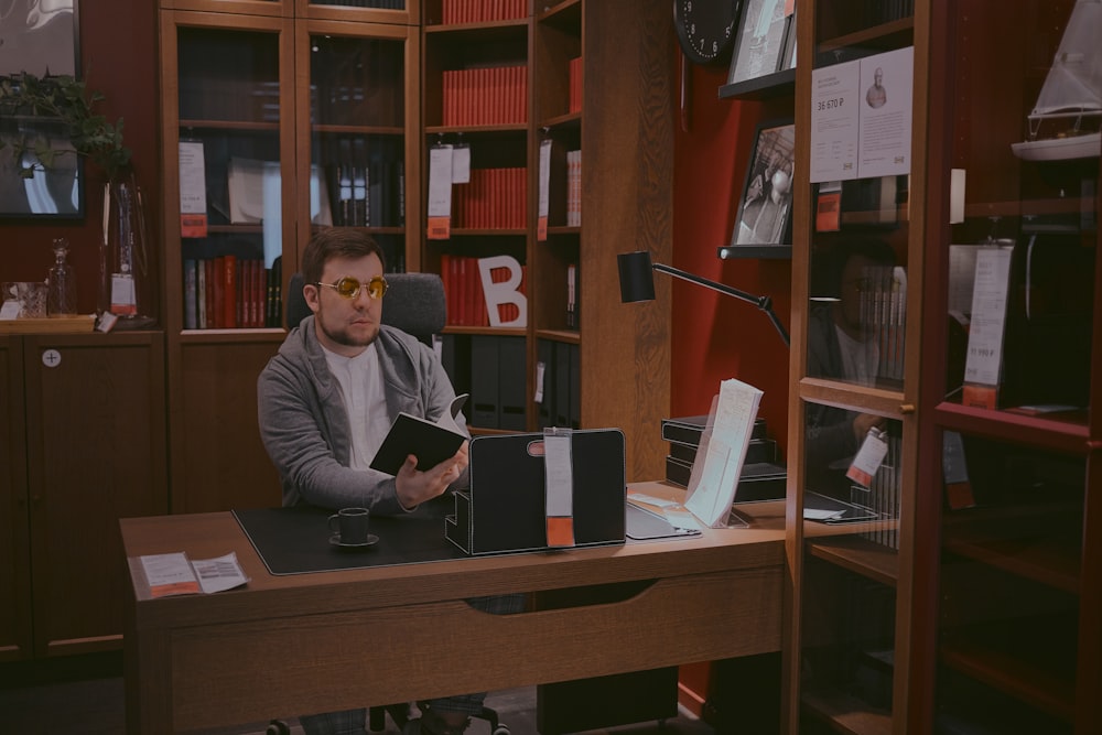 man in gray sweater sitting beside brown wooden desk