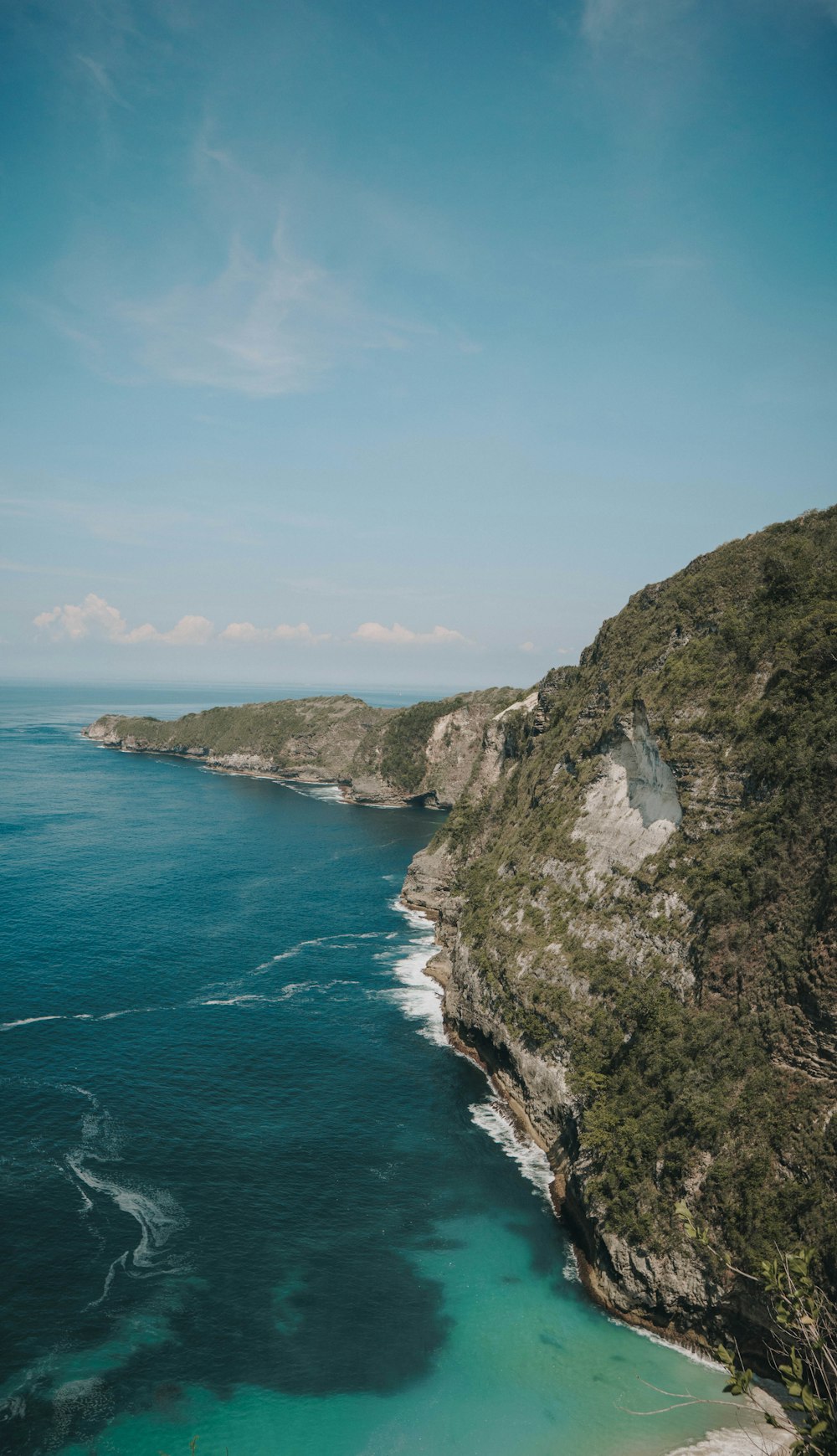 green and brown mountain beside blue sea under blue sky during daytime