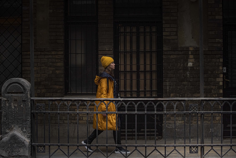 person in yellow and black coat standing near brown brick wall