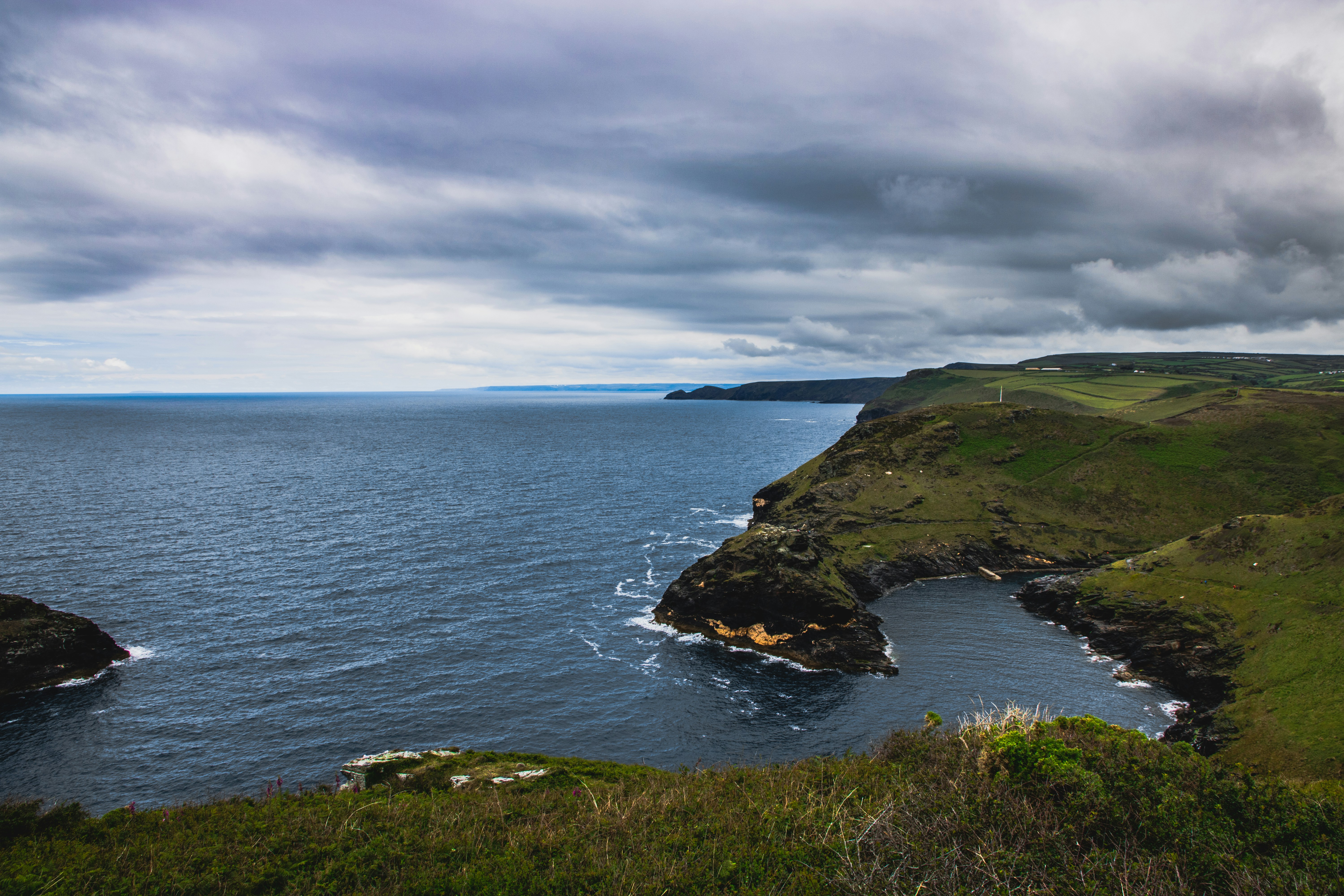 green grass field beside body of water under cloudy sky during daytime