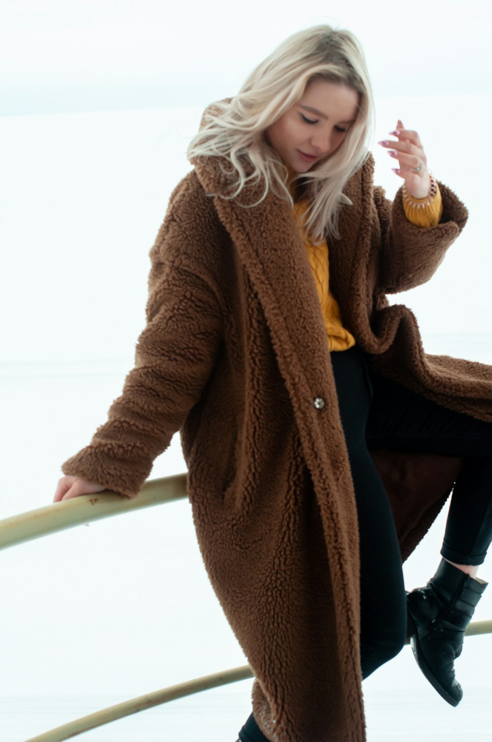 woman in brown coat and black pants sitting on white chair