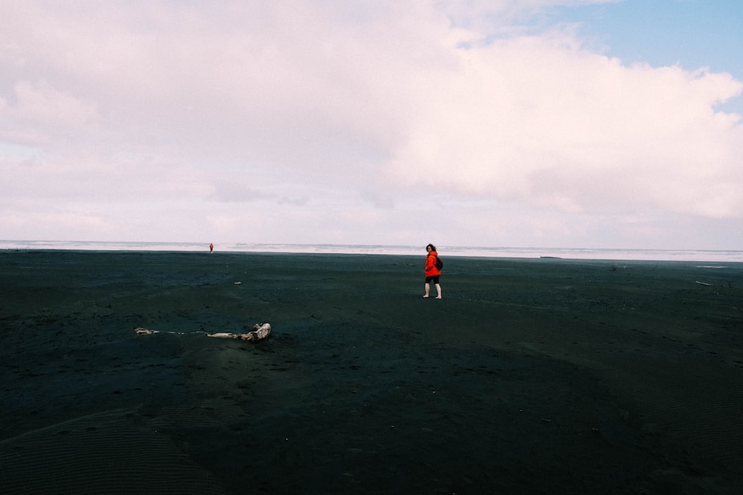 person in red jacket and black pants standing on seashore during daytime