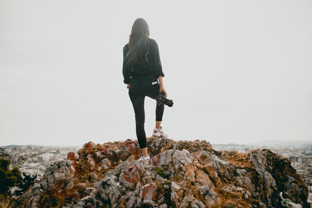 femme en veste noire debout sur la montagne rocheuse marron pendant la journée