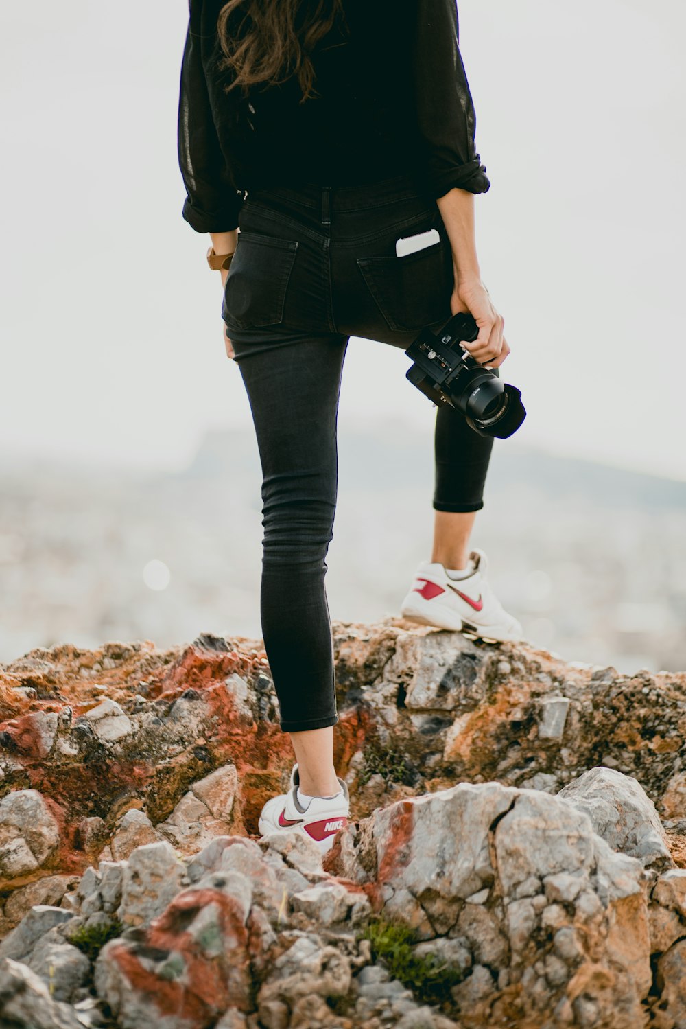 Donna in camicia nera e pantaloni neri che tiene la fotocamera DSLR nera