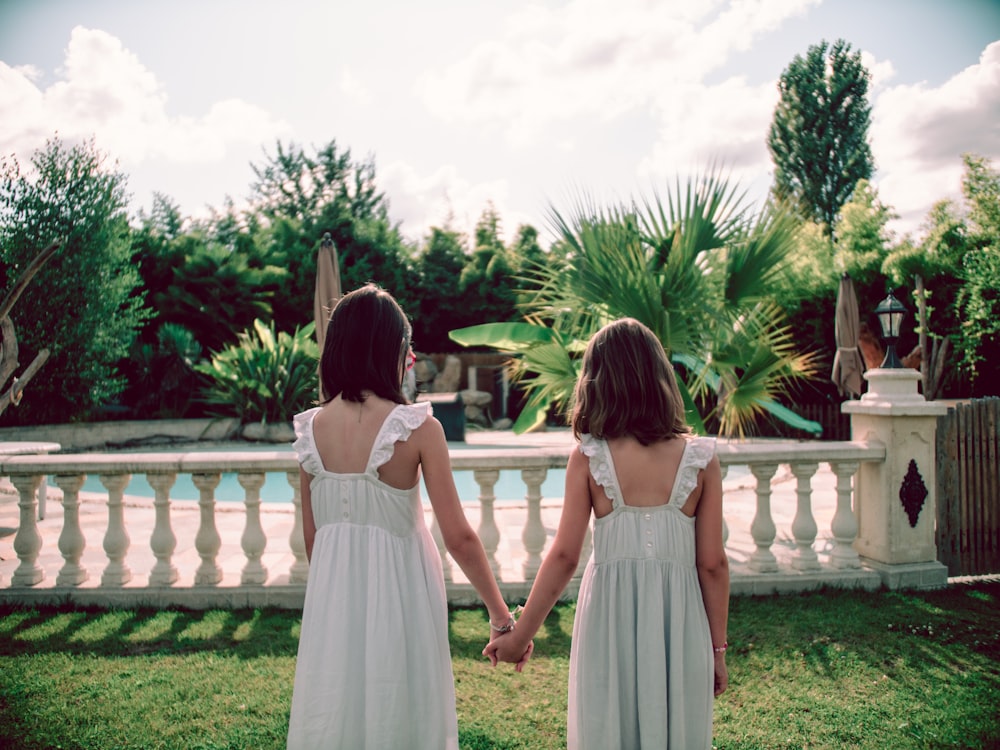 2 girls in white dresses standing on green grass field during daytime