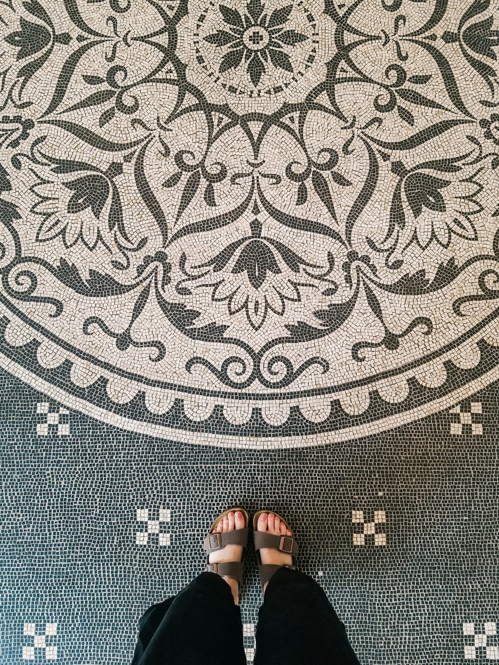 person wearing black flip flops standing on gray and black area rug