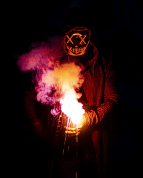person in black mask holding purple and pink smoke