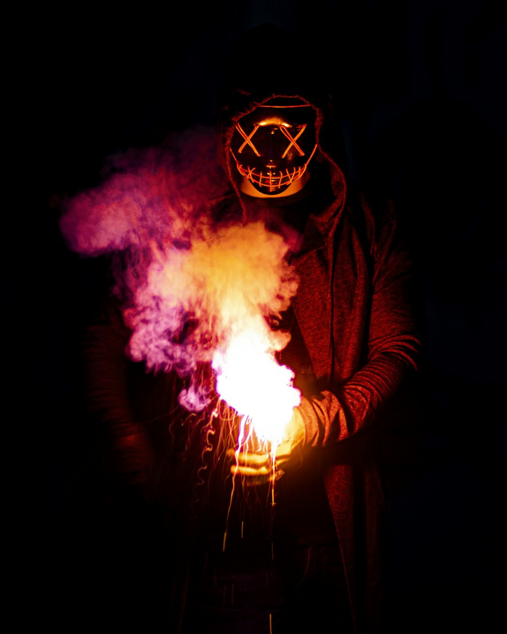 person in black mask holding purple and pink smoke