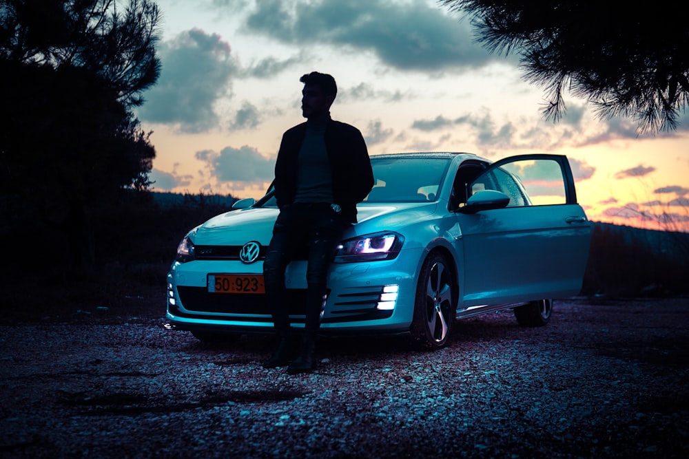 man in black jacket and pants standing beside blue bmw car