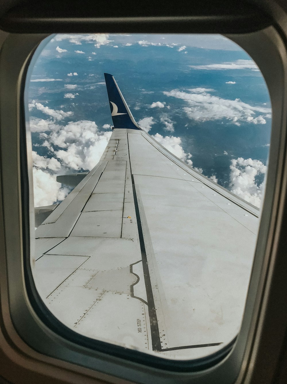 white and gray airplane wing under white clouds and blue sky during daytime