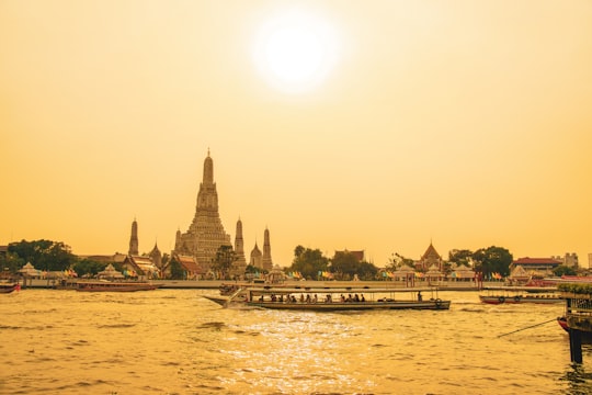 people walking on bridge over body of water during daytime in Wat Arun Thailand