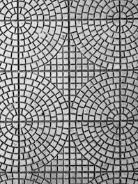 An intricate pattern of circular and square shapes on a textured surface. The design consists of evenly spaced concentric circles intersected by straight lines, creating a symmetrical and geometric appearance.