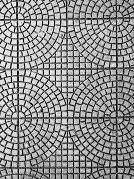 An intricate pattern of circular and square shapes on a textured surface. The design consists of evenly spaced concentric circles intersected by straight lines, creating a symmetrical and geometric appearance.