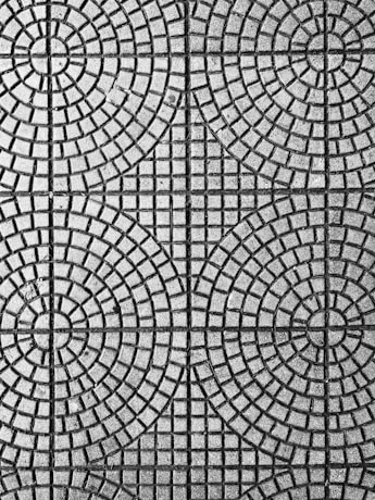An intricate pattern of circular and square shapes on a textured surface. The design consists of evenly spaced concentric circles intersected by straight lines, creating a symmetrical and geometric appearance.