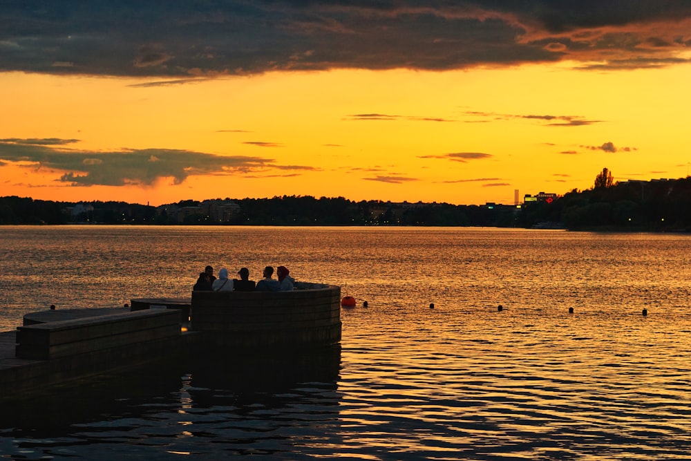 silhouette of 2 people sitting on dock during sunset