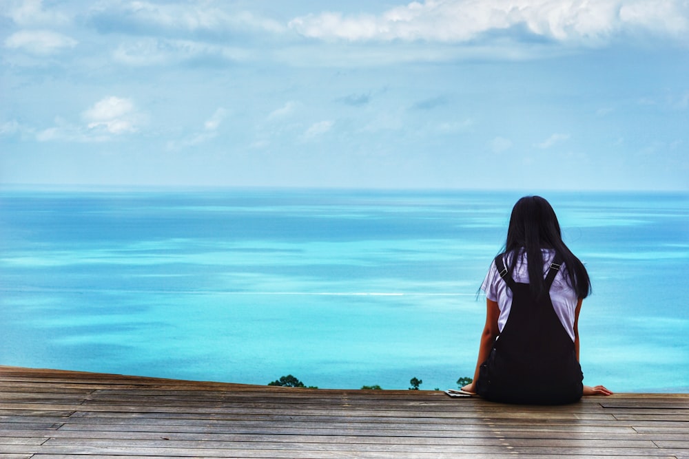 woman in black shirt standing on wooden dock by the sea during daytime