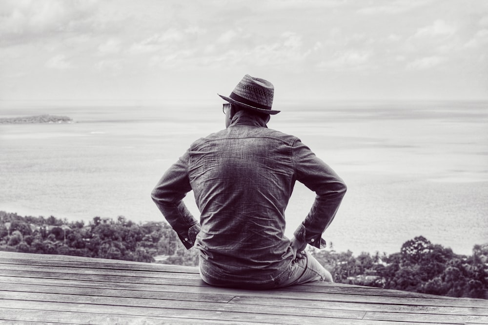 man in gray hoodie and black hat sitting on wooden dock