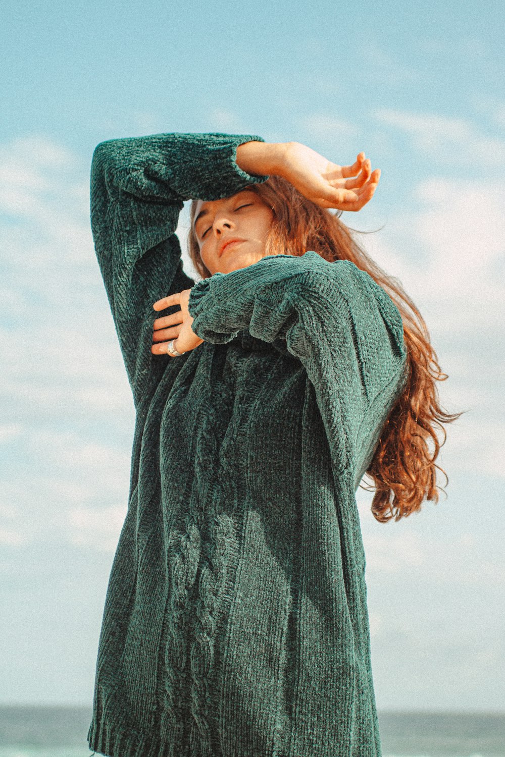 woman in blue sweater covering her face with her hand