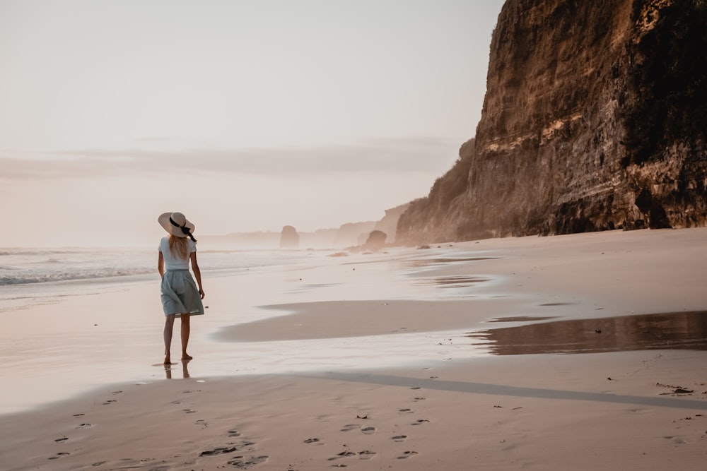 woman in white shirt and blue denim shorts walking on beach during daytime