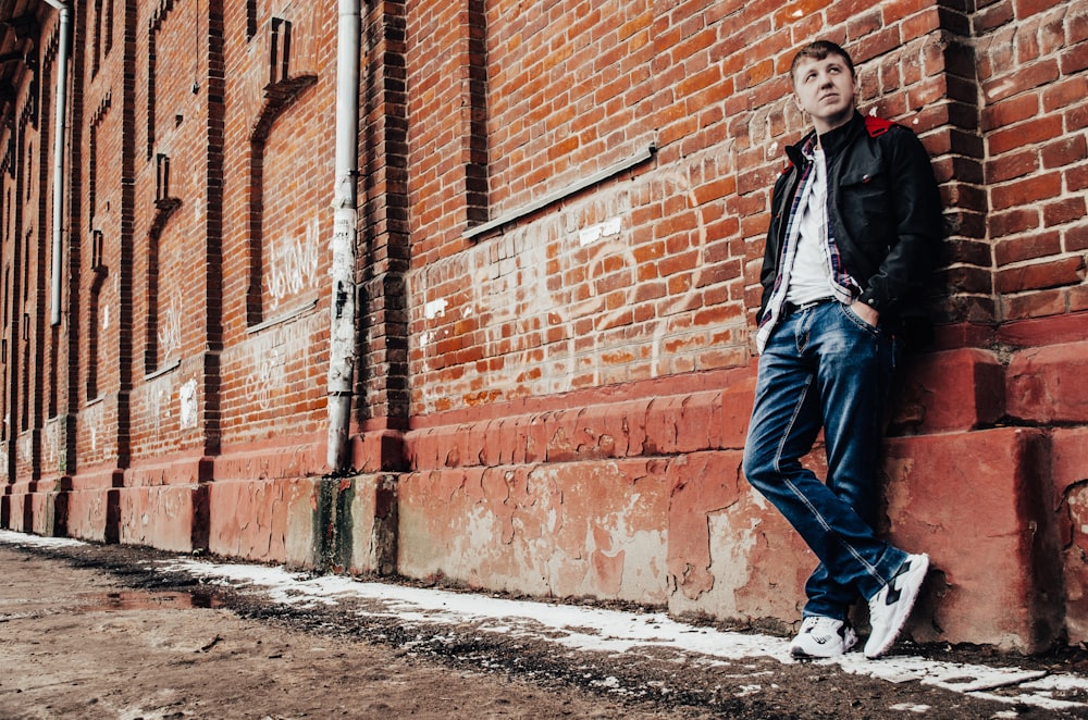 woman in black jacket and blue denim jeans standing beside brown brick wall during daytime