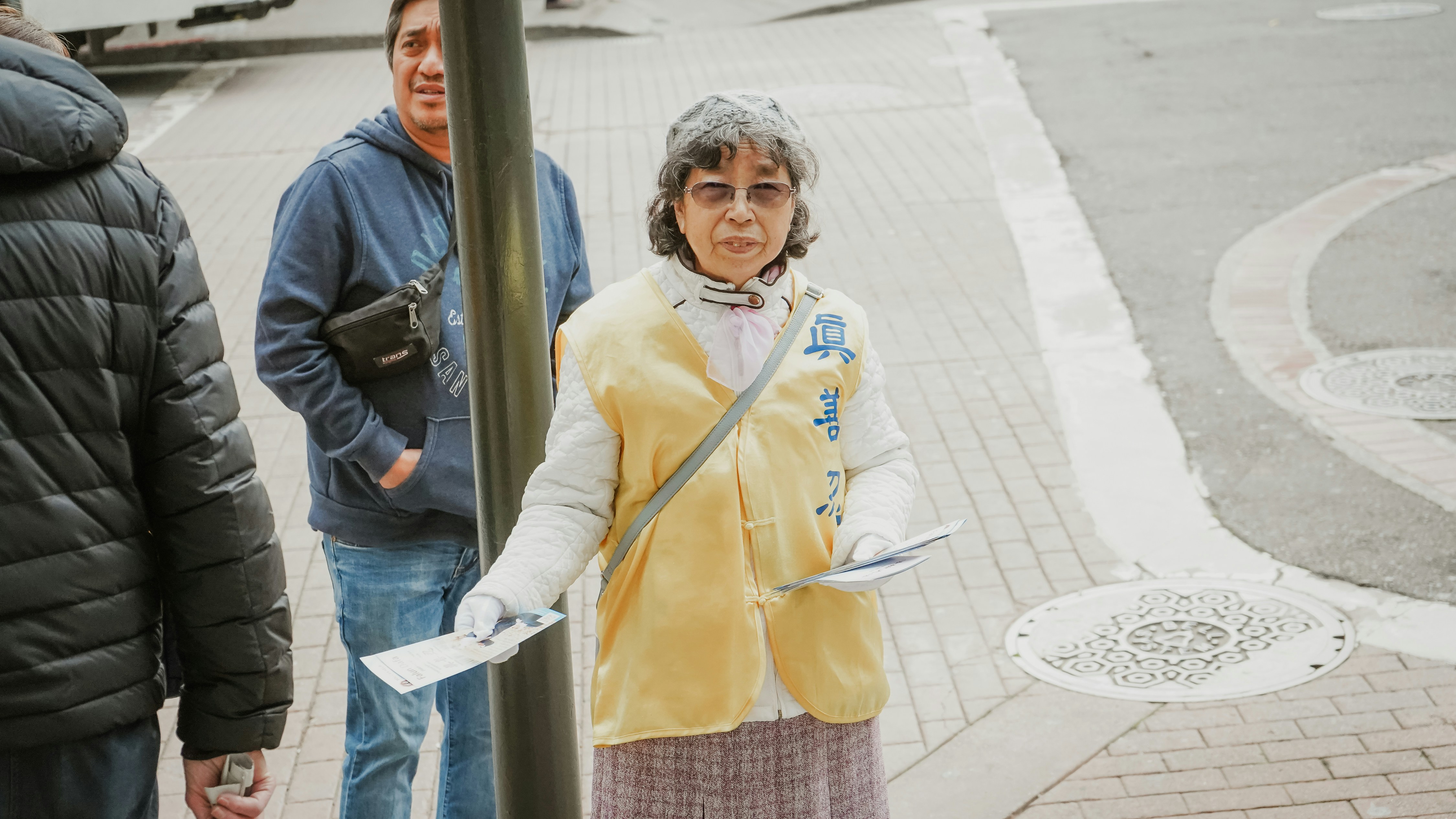 Frau in gelber Jacke und blauer Jeans neben grauem Metallpfosten