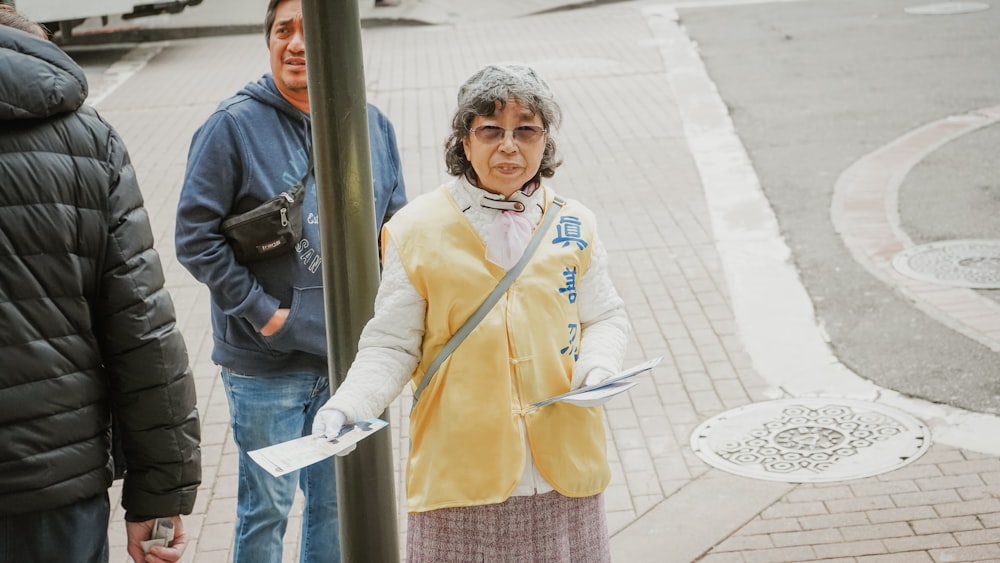 woman in yellow jacket and blue denim jeans standing beside gray metal post