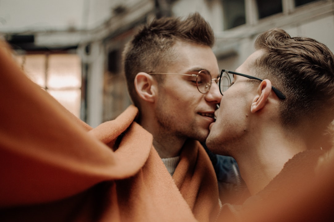 man in black framed eyeglasses kissing woman in red dress