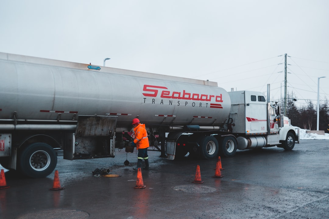 man in orange jacket and black pants standing on red and white freight truck during daytime