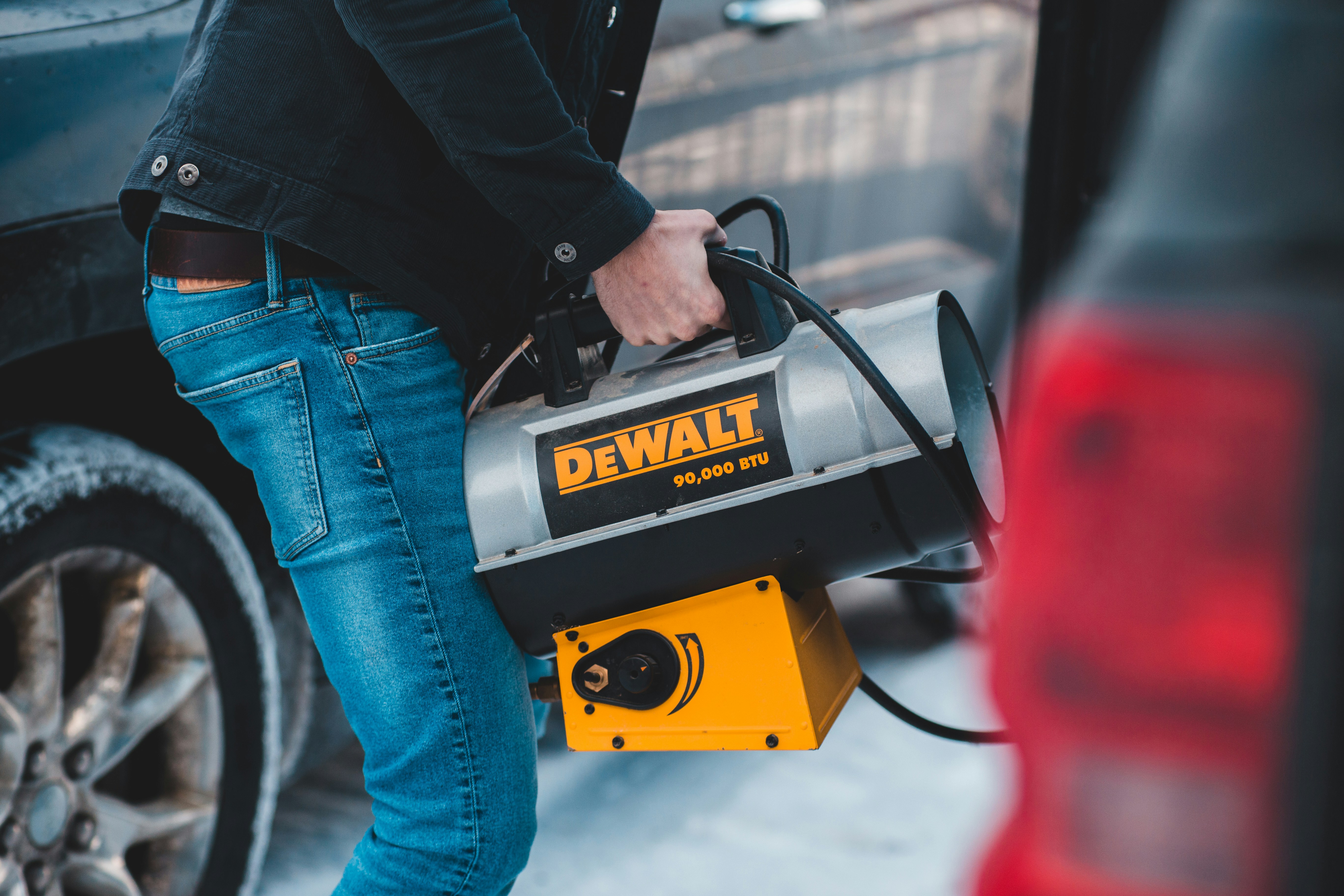 person in black jacket and blue denim jeans holding yellow and black UNK power tool