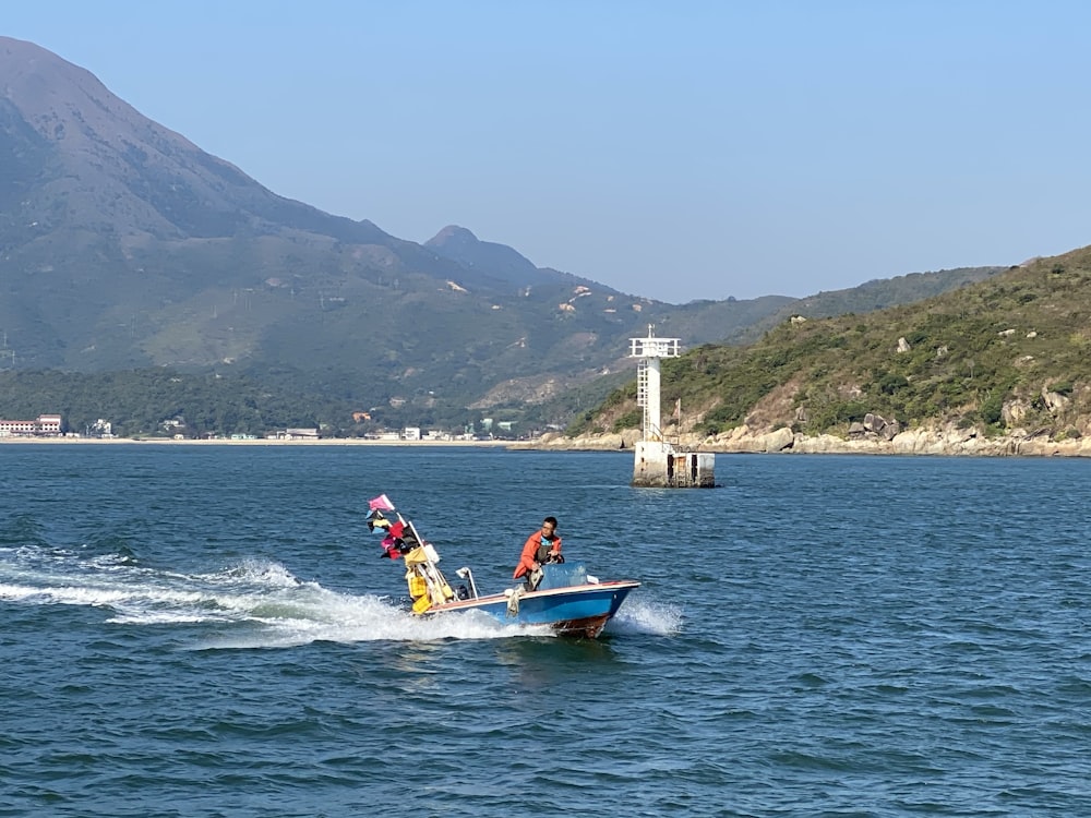 man in red shirt riding on blue and white boat on sea during daytime