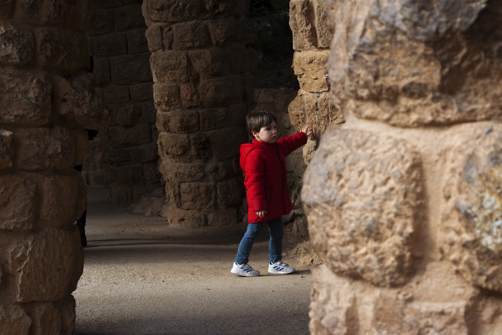 child in red jacket and blue denim jeans walking on gray asphalt road during daytime