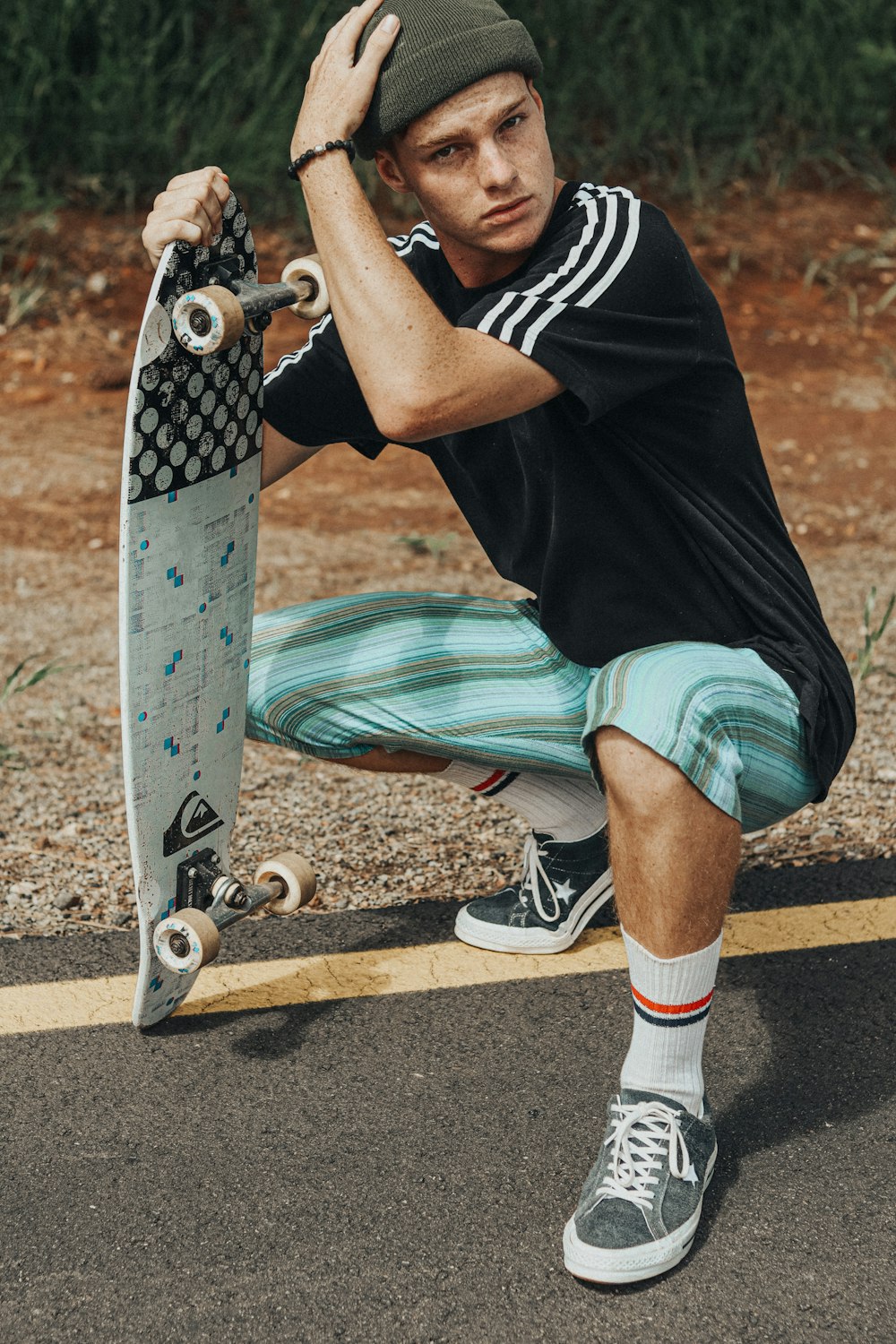 man in black and white shirt and green shorts sitting on skateboard during daytime