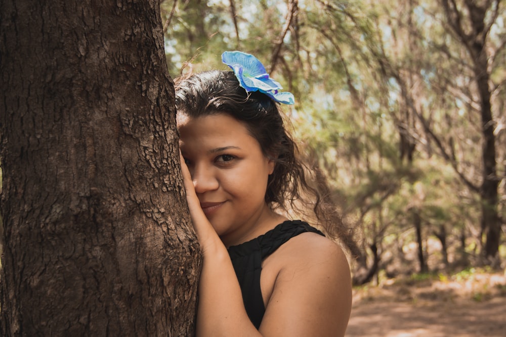 girl in black tank top leaning on brown tree during daytime