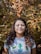 woman in white and blue crew neck shirt standing beside green and brown leaves