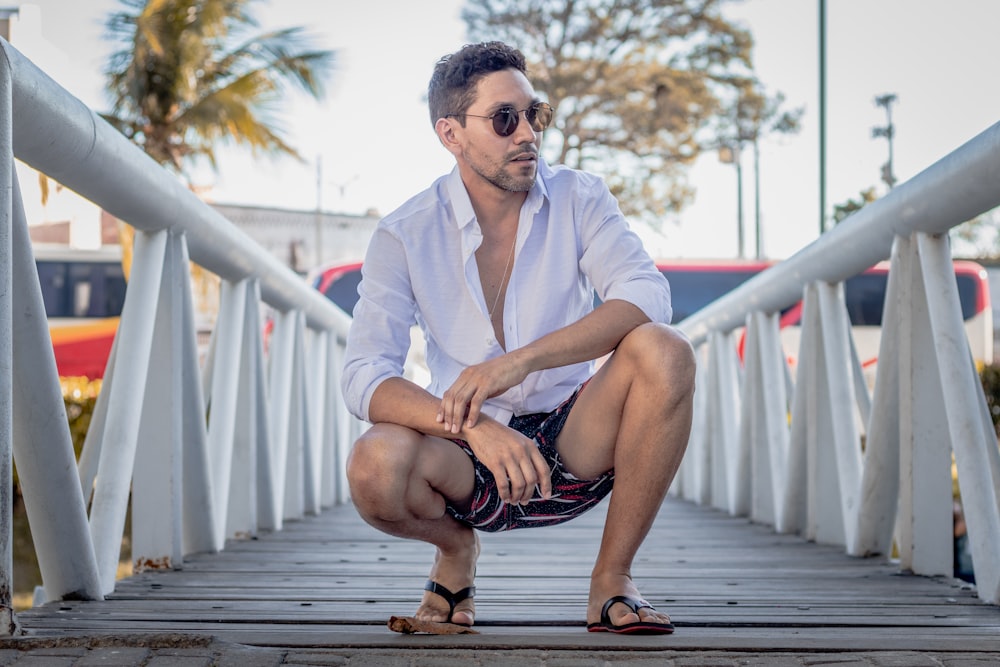 man in white dress shirt sitting on wooden bridge during daytime