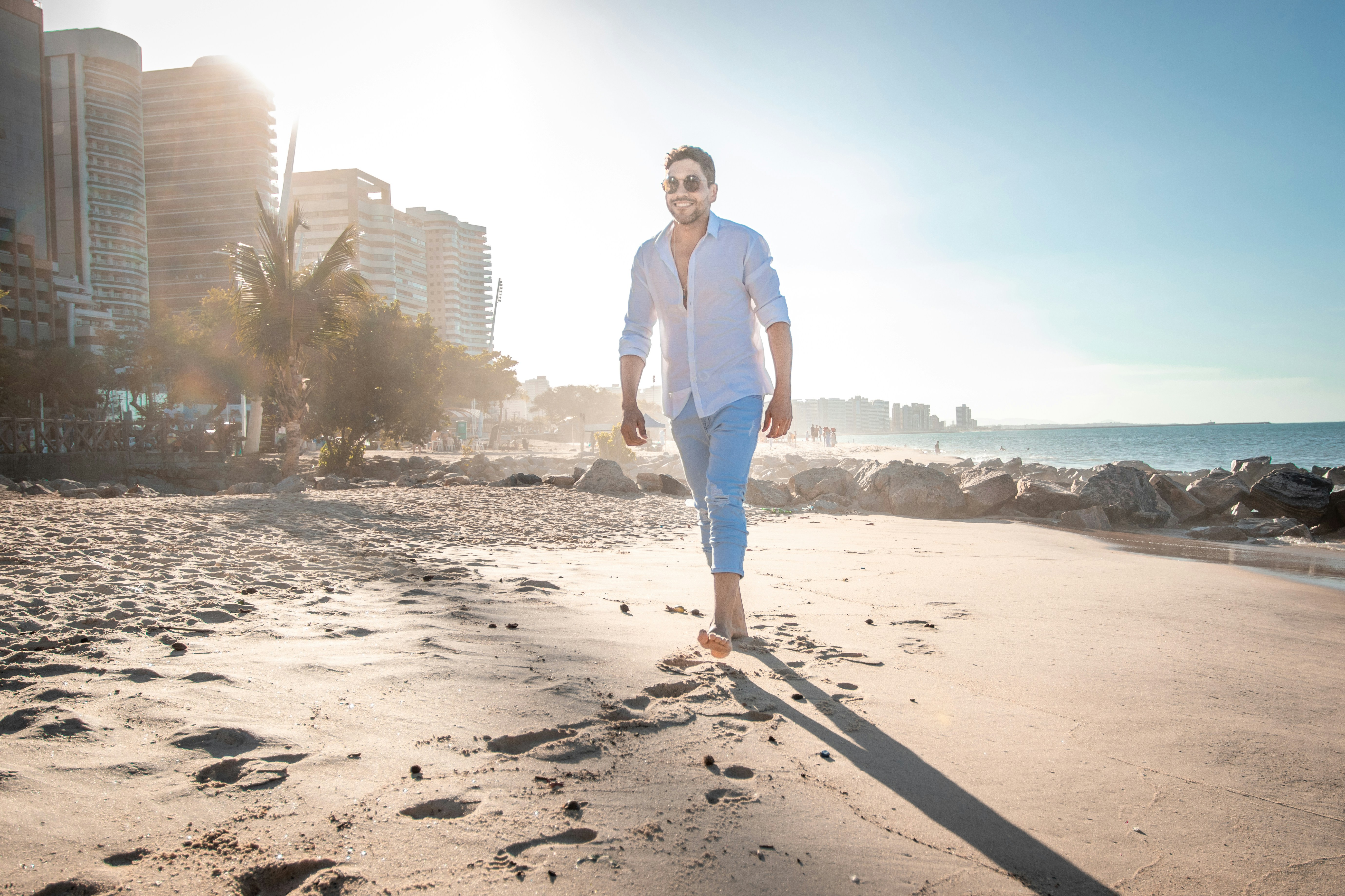 man in white dress shirt and blue denim jeans standing on beach shore during daytime